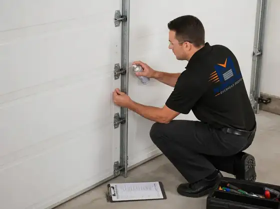 Technician lubricating garage door hinges and rollers during a maintenance inspection